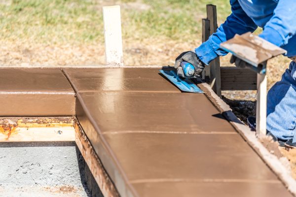 Construction Worker Using Trowel On Wet Cement Forming Coping Around New Pool.