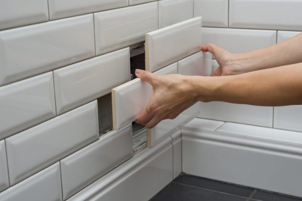 Woman opens, closes the hidden revision sanitary hatch on the wall of tile under the bathroom